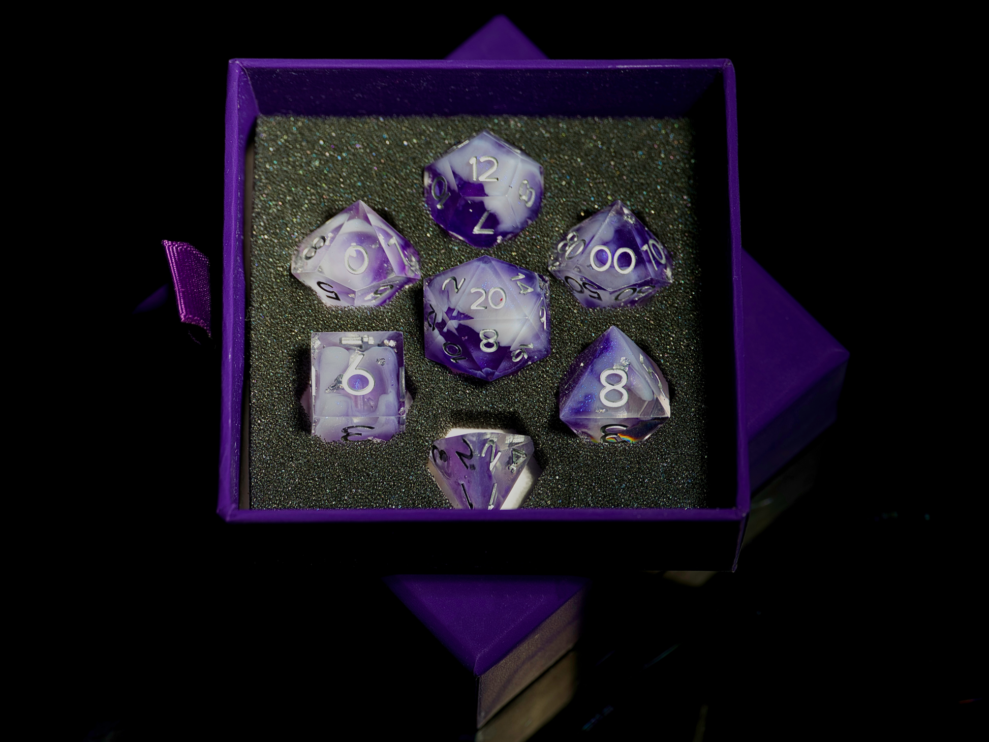 Set of purple polyhedral dice in a purple box on a black background